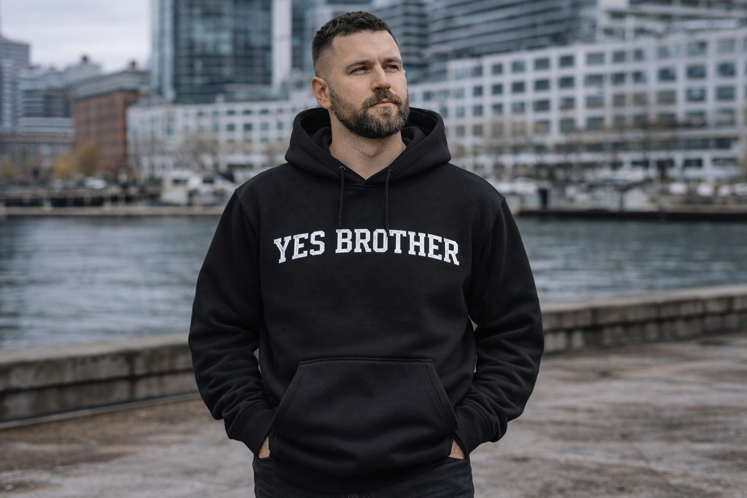 Man wearing black 'YES BROTHER' hoodie outdoors by waterfront